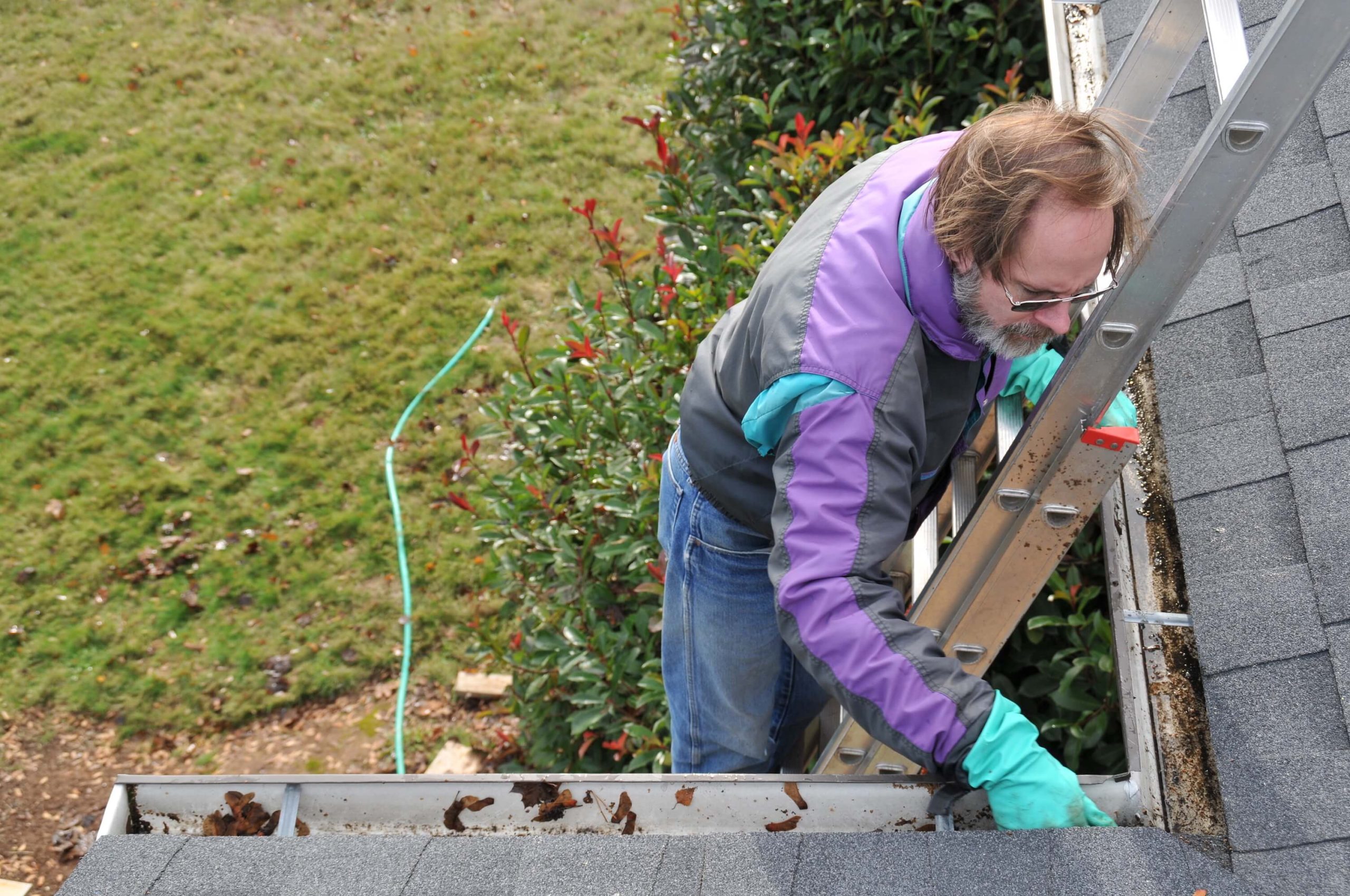older man in a purple teal and black jacket cleaning gutters